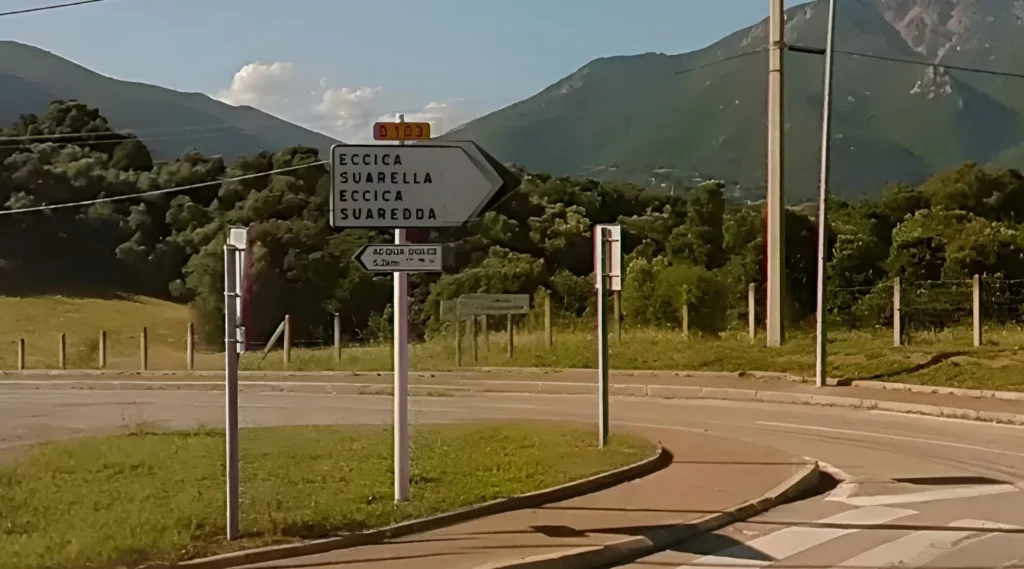 Panneau directionnel vers Eccica-Suarella à un carrefour routier, route départementale et relief montagneux en arrière-plan.