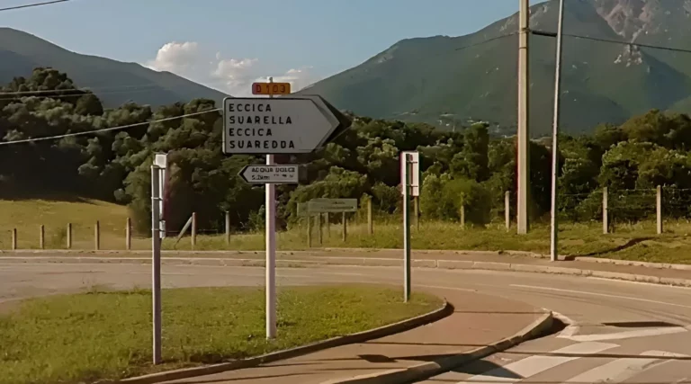 Panneau directionnel vers Eccica-Suarella à un carrefour routier, route départementale et relief montagneux en arrière-plan.